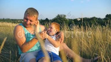 快乐的年轻人躺在草地上和他的小男孩玩耍。 父亲在户外给他的小儿子挠痒痒